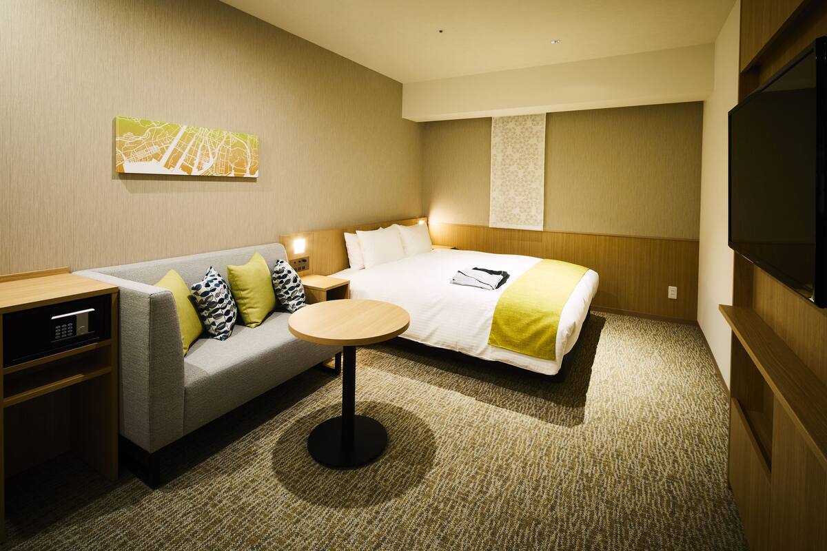 Una habitación de hotel con cama, sofá, una mesita y televisión.