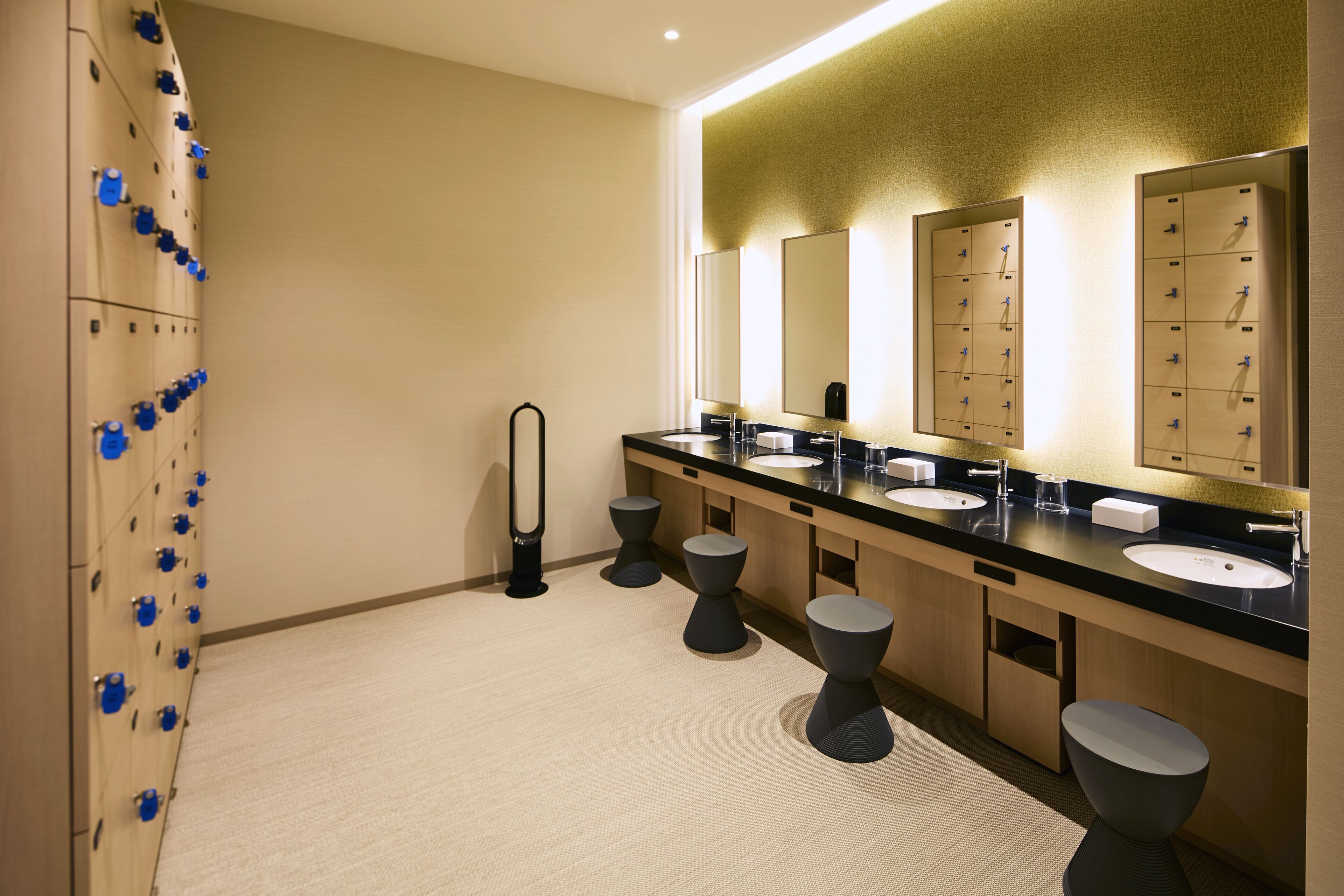 A modern bathroom with three sinks, a large mirror, and a towel rack with blue towels.