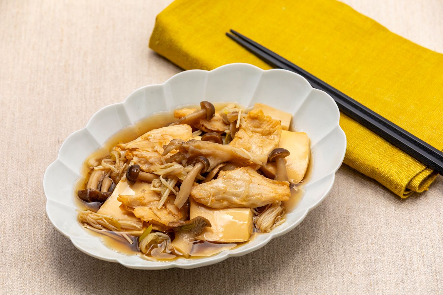 A bowl of food with chopsticks and a yellow napkin on a textured surface.