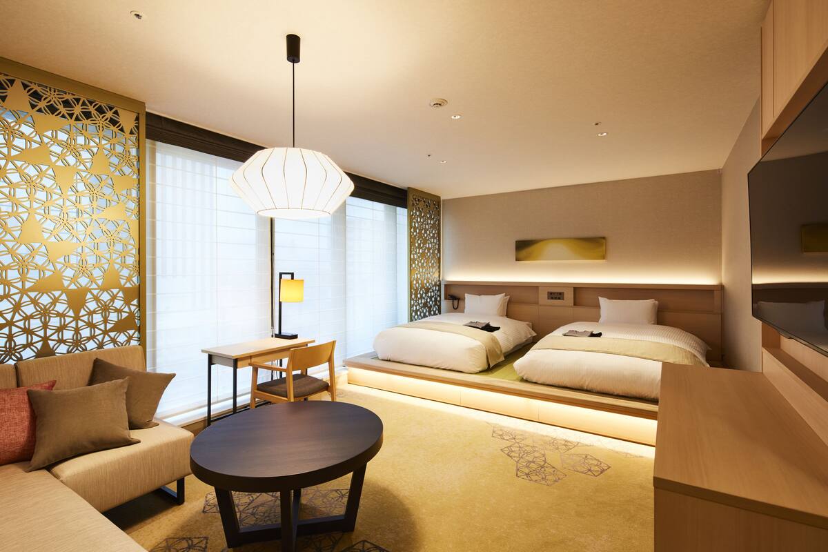 Una habitación de hotel moderna con sofá, una mesa redonda, un escritorio y dos camas.