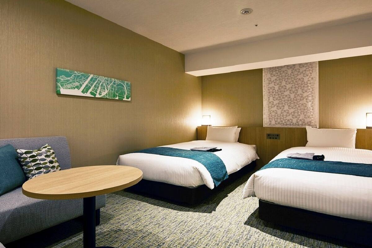 Habitación de hotel con dos camas, un sofá, una mesa redonda y un mapa en la pared.