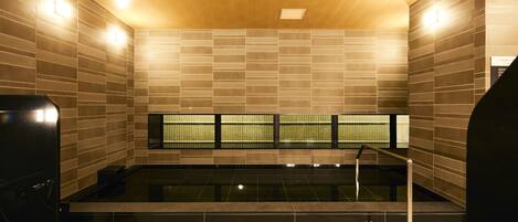 Un moderno espacio de spa con una bañera de hidromasaje negra, techo de madera y paredes de azulejos.
