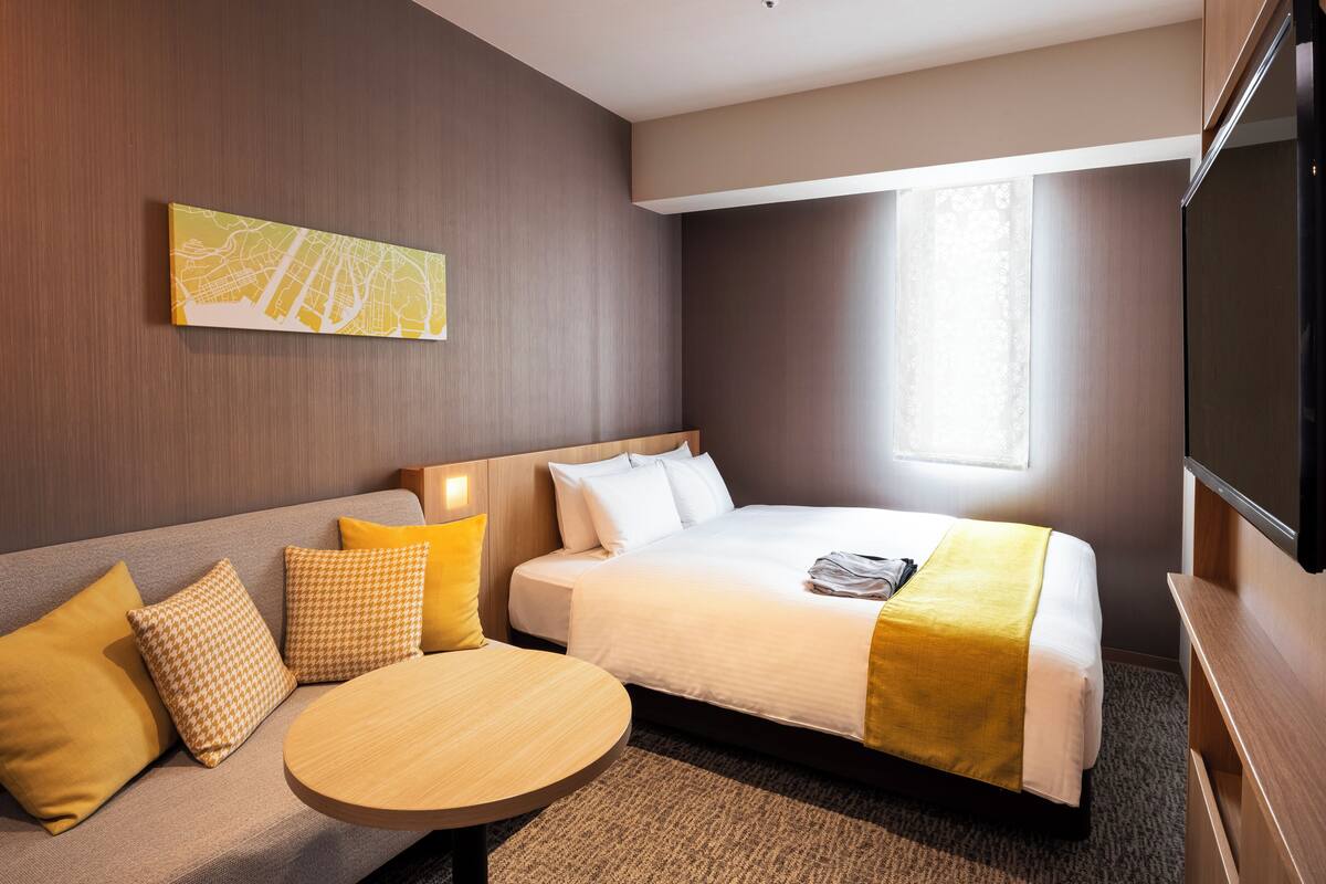 Una habitación de hotel con cama, sofá, mesa redonda y televisor.