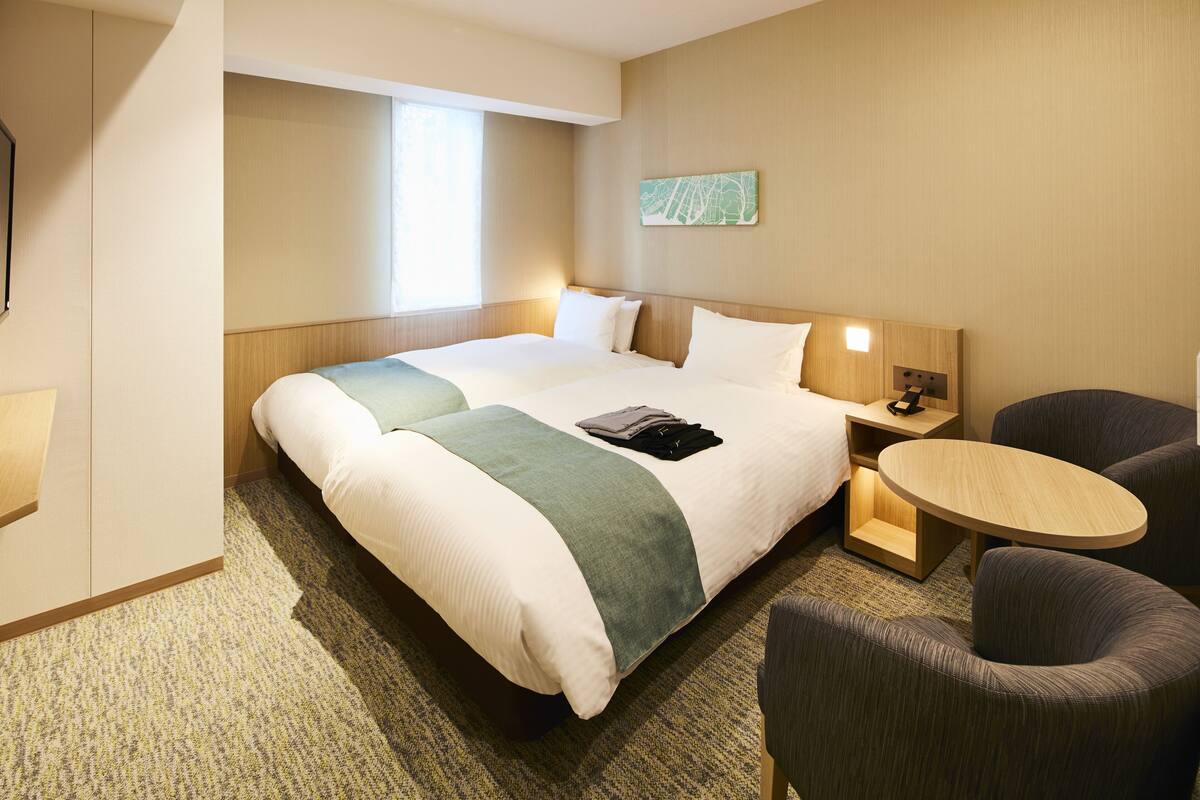 Una habitación de hotel con una cama grande, una mesita pequeña, una silla y una mesita de noche.