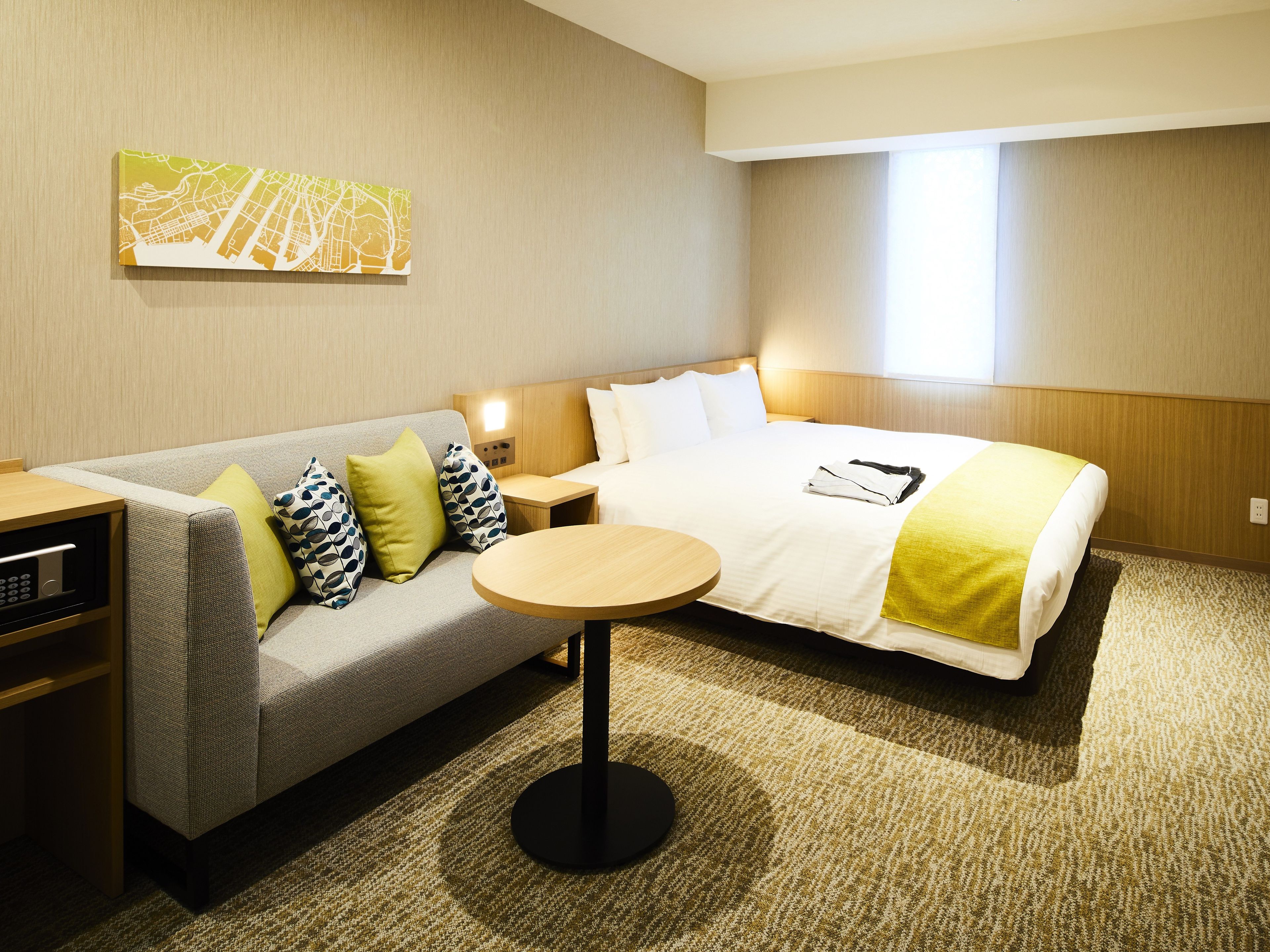 A hotel room with a bed, a sofa, a bedside table, a lamp, and a carpeted floor.
