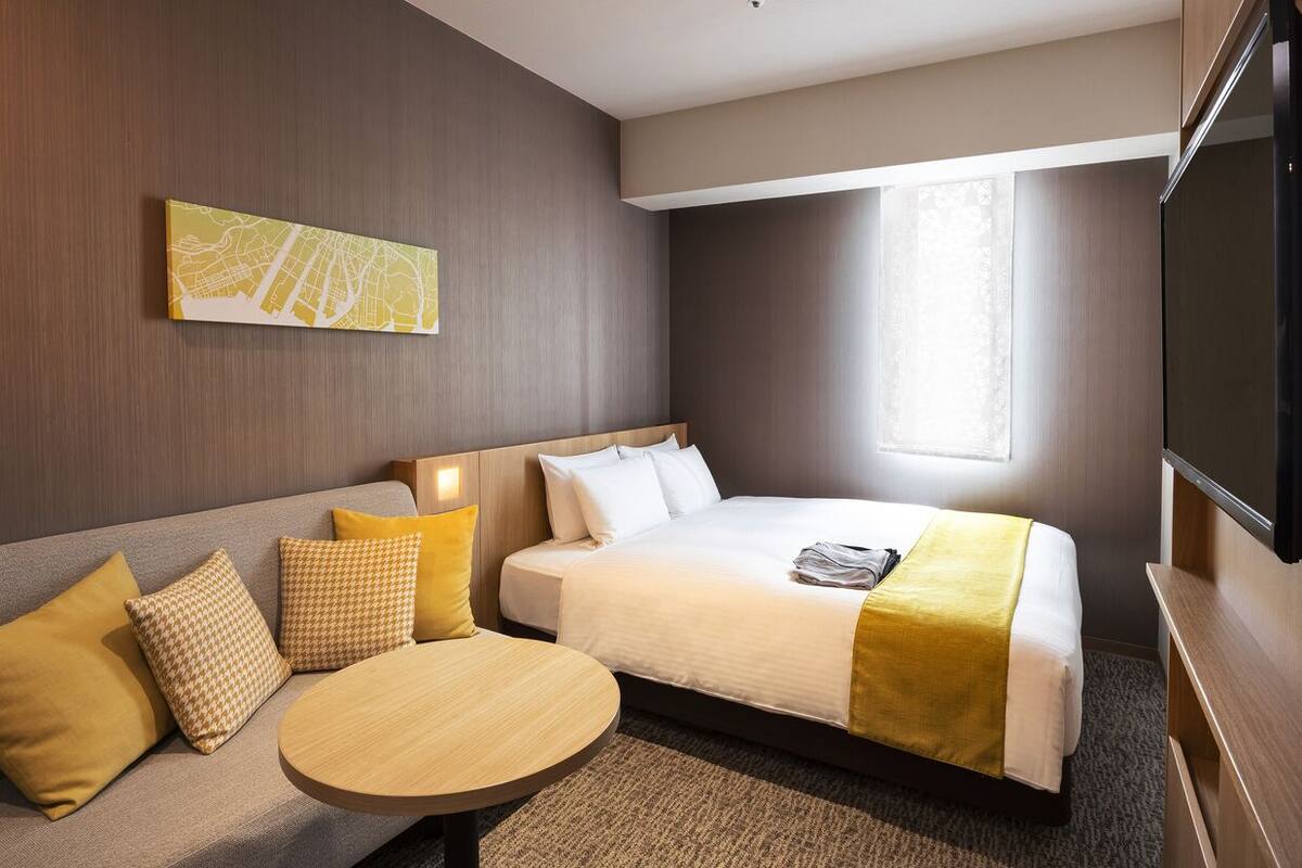 Una habitación de hotel con cama, sofá, mesa redonda y un cuadro con un mapa en la pared.