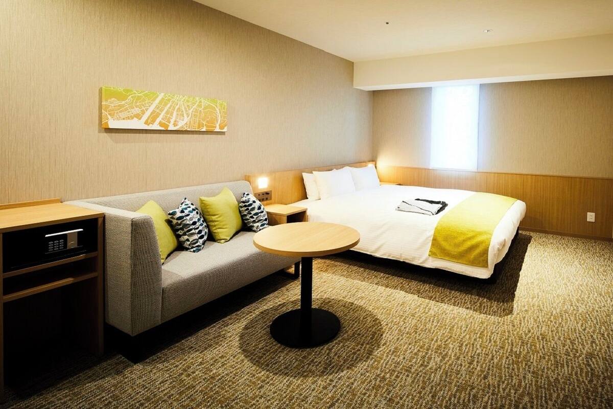 Habitación de hotel con cama, sofá, una pequeña mesa redonda, televisor y una obra de arte en la pared.