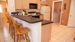Una cocina con una isla central, taburetes de madera, microondas, refrigerador y lavadora.