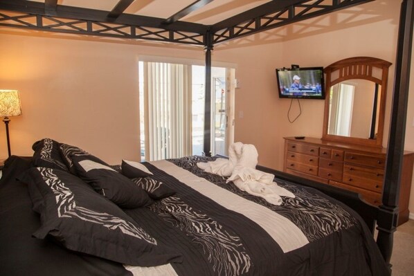 A bedroom with a bed, a television mounted on the wall, a dresser, and a window with blinds.