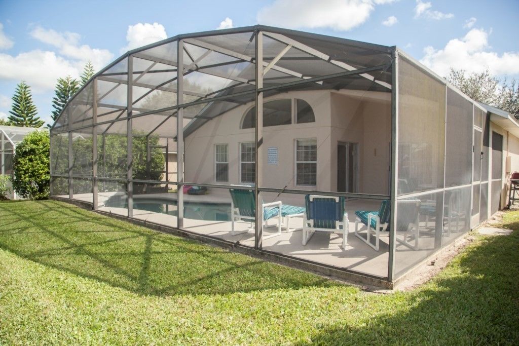 Un espacio al aire libre techado con una piscina, sillas de descanso y una casa al fondo.