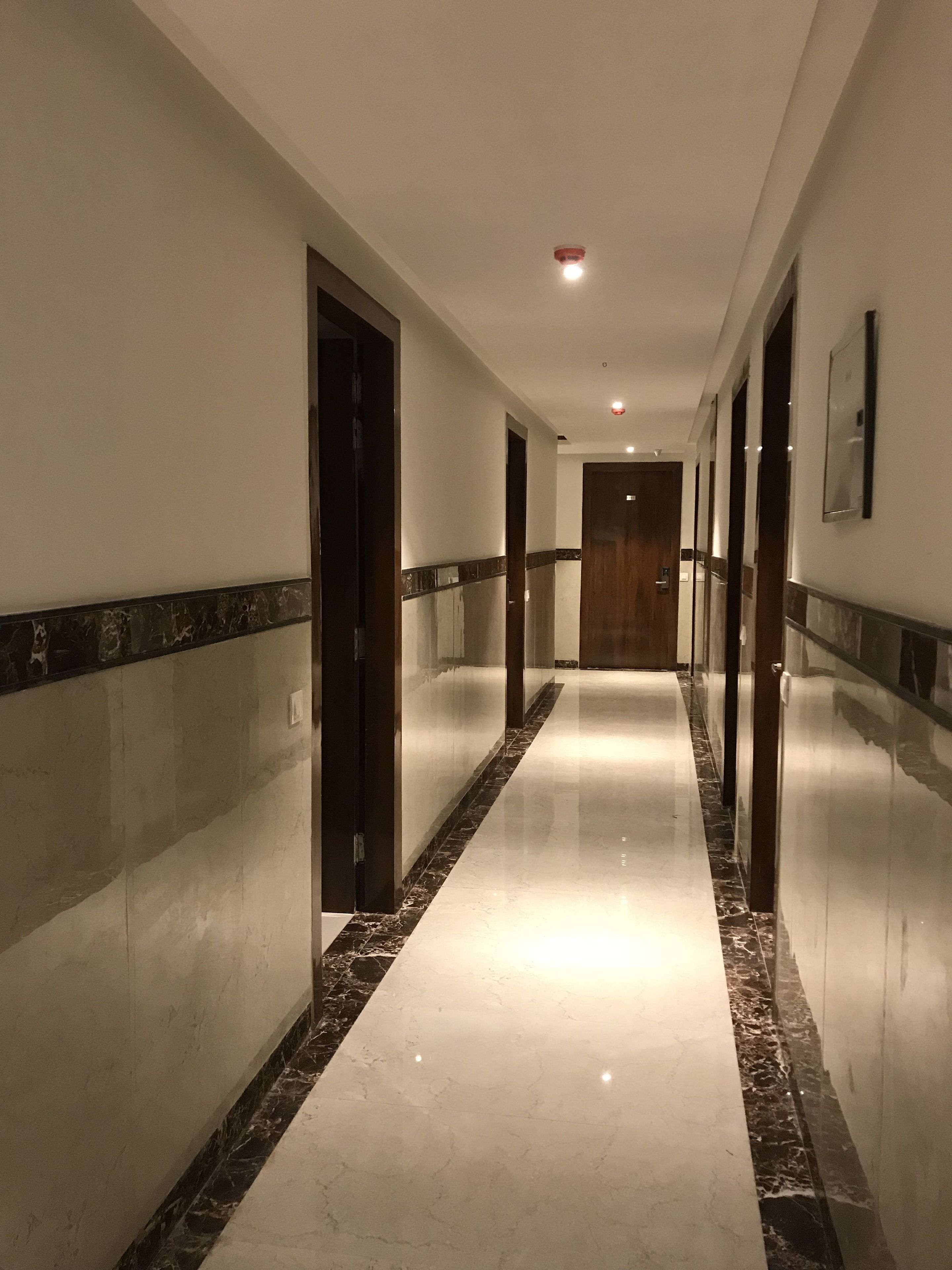 A long, well-lit hallway with marble flooring and wooden doors.