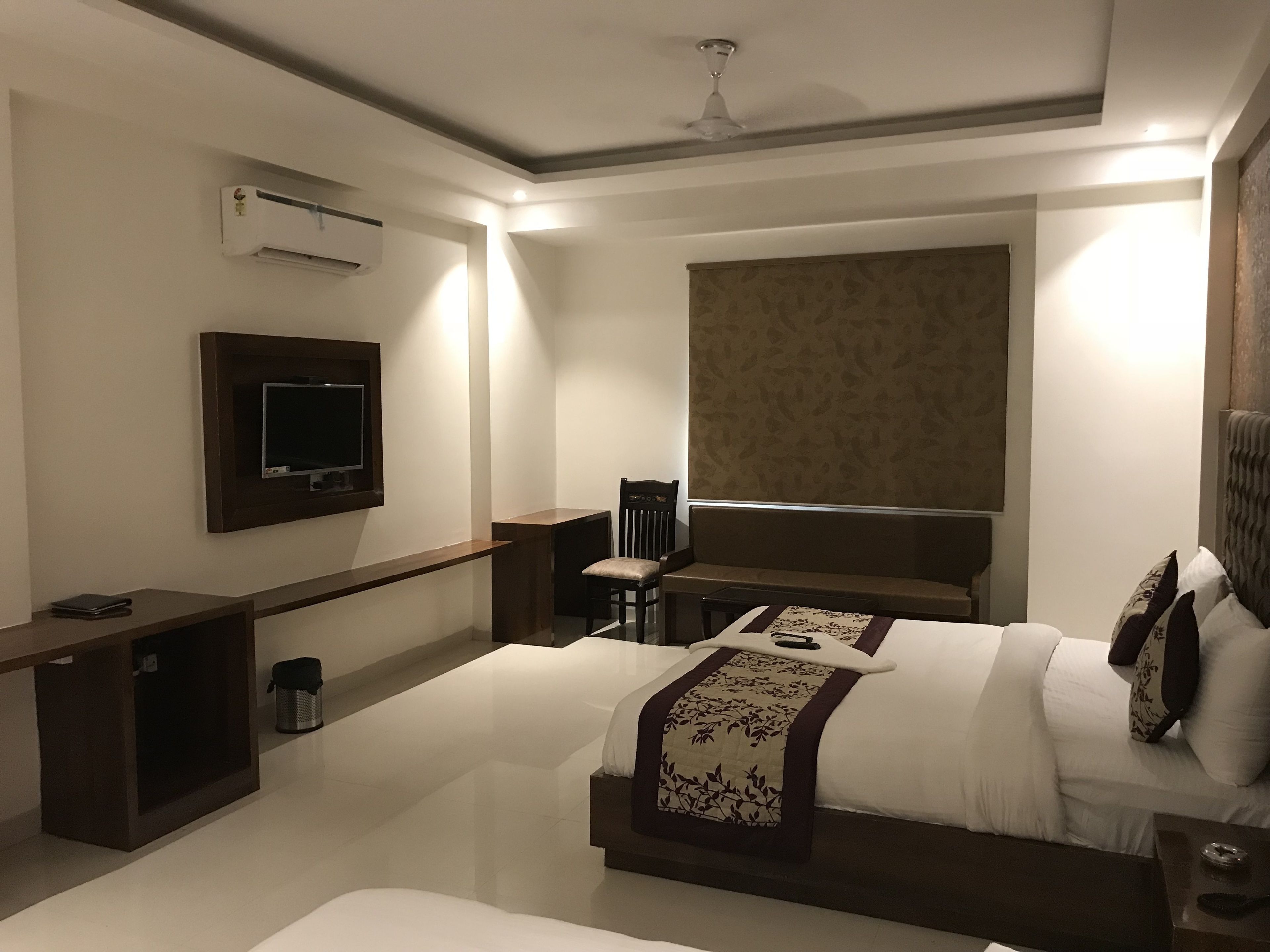 A modern hotel room with a large bed, a TV mounted on the wall, and a ceiling fan.