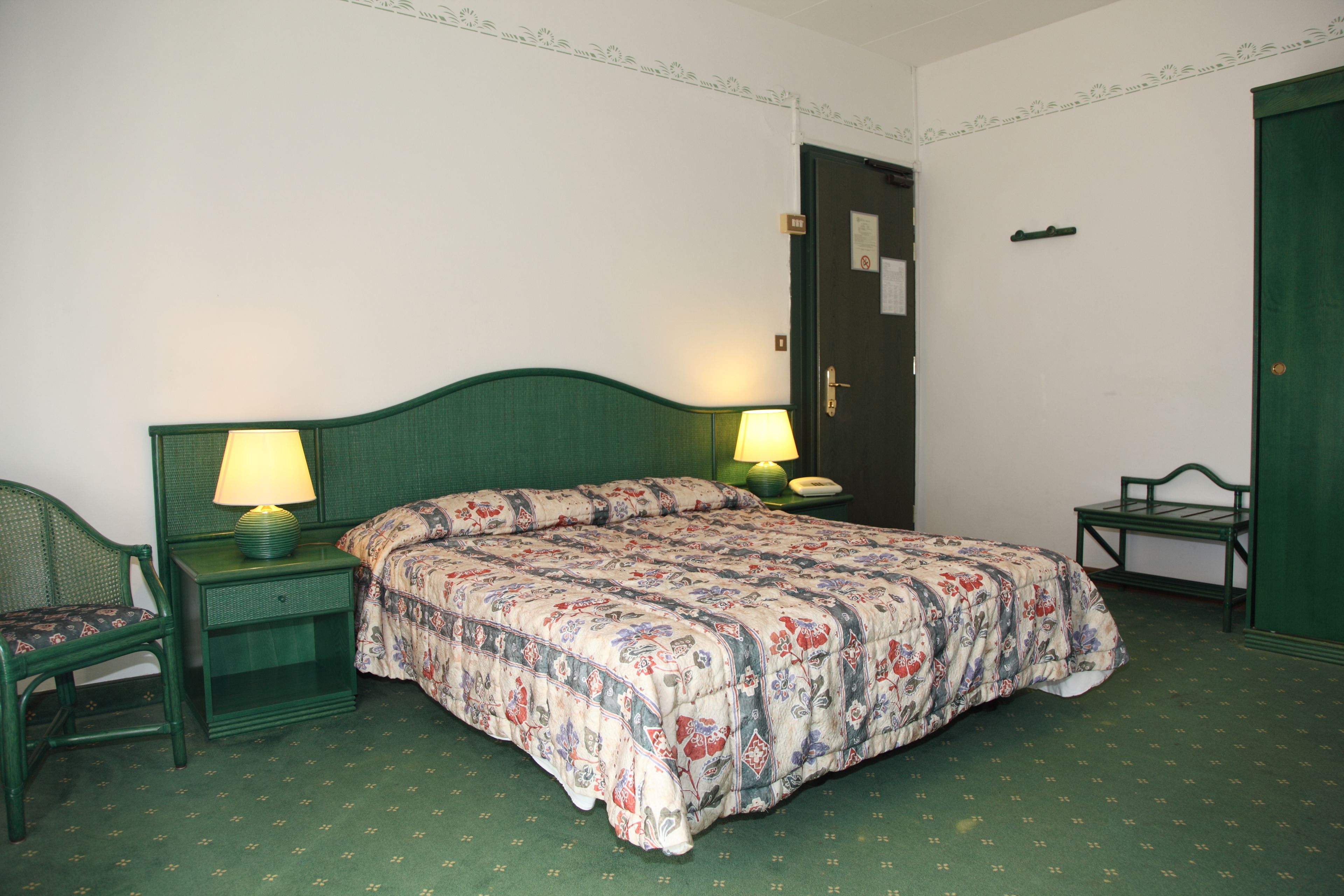 A neatly arranged bedroom with a single bed, two bedside tables with lamps, a chair, and a green wardrobe.