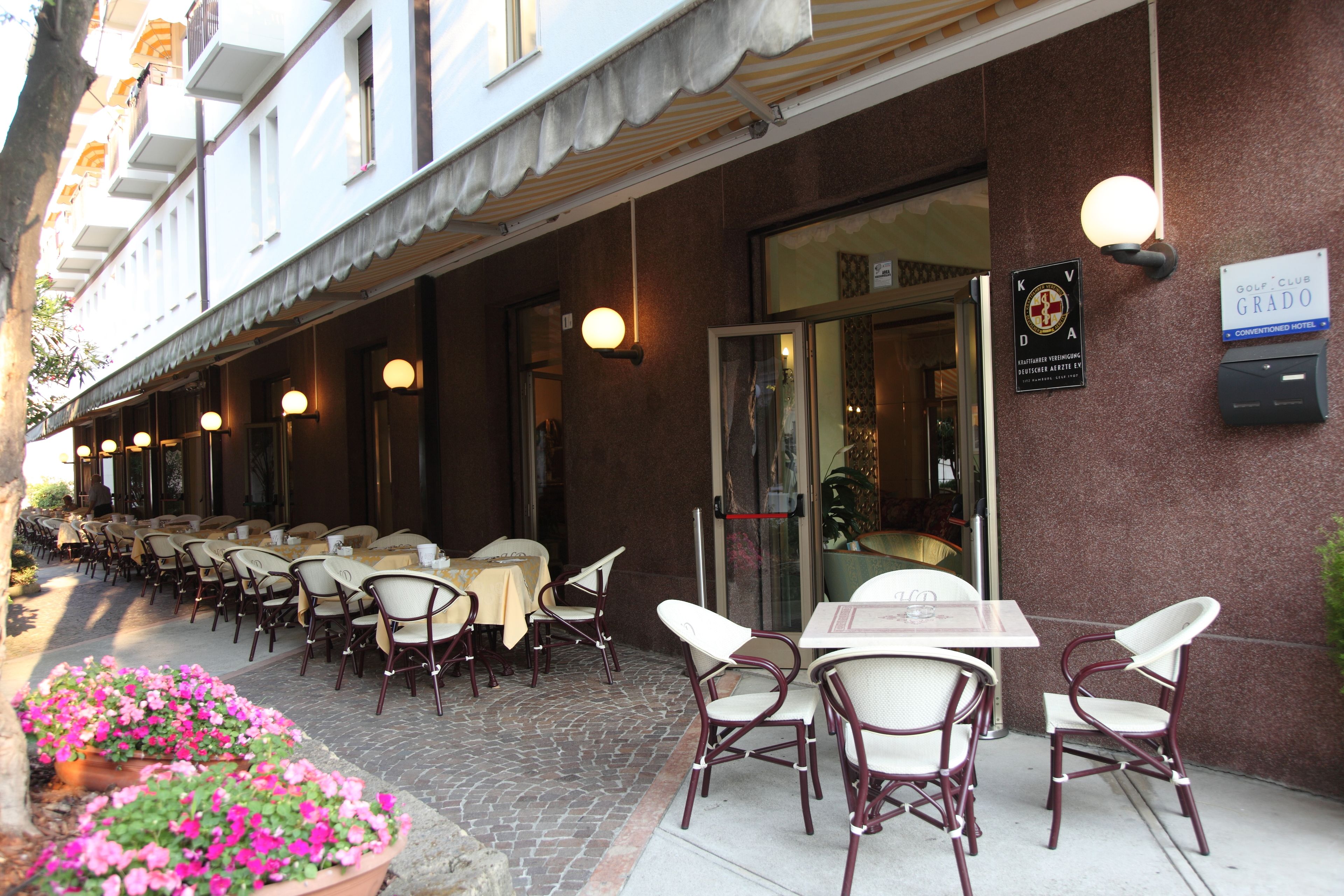 Um café ao ar livre com mesas e cadeiras, um canteiro de flores e um edifício com uma placa.