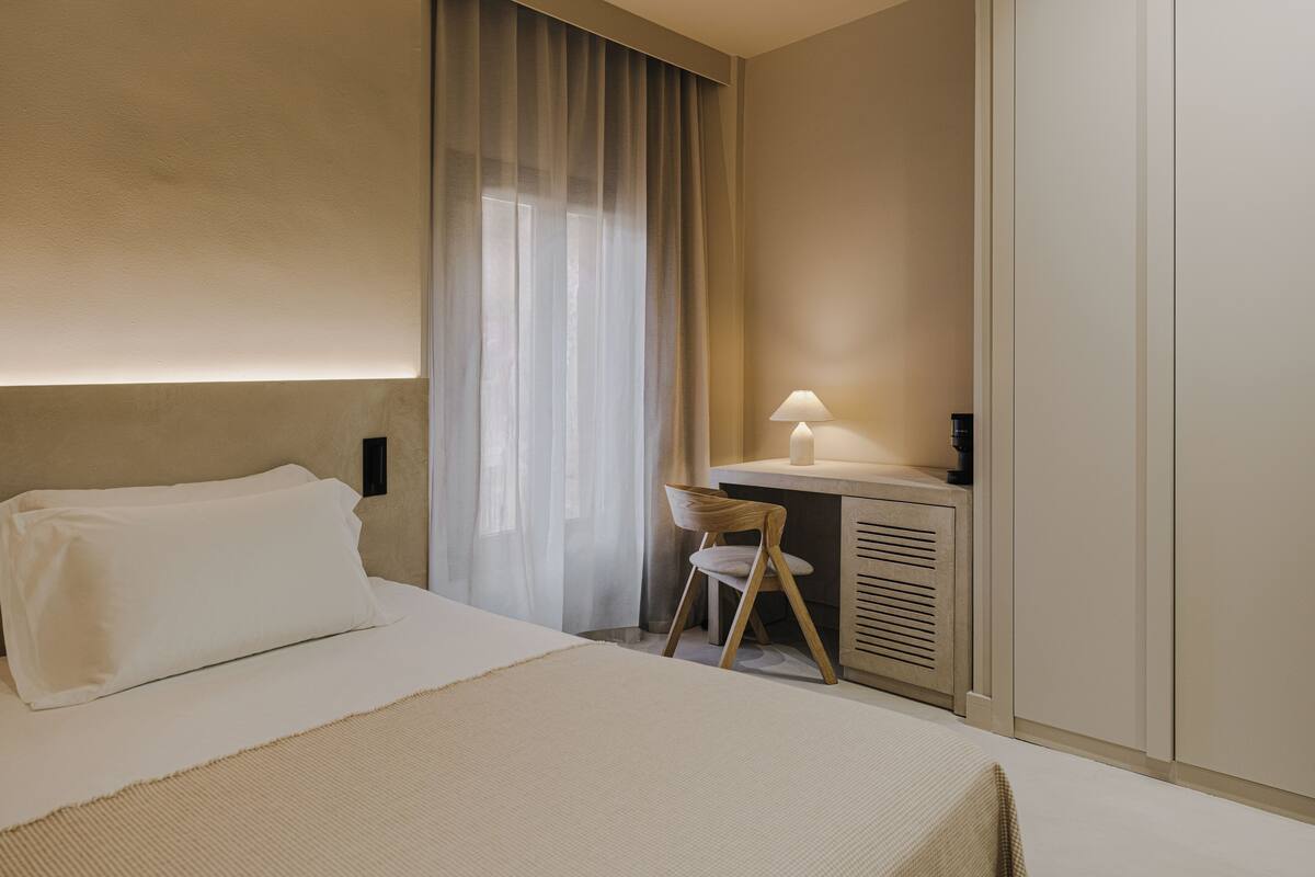 Une chambre d’hôtel comprenant un lit, un bureau avec une lampe, une chaise et une armoire.