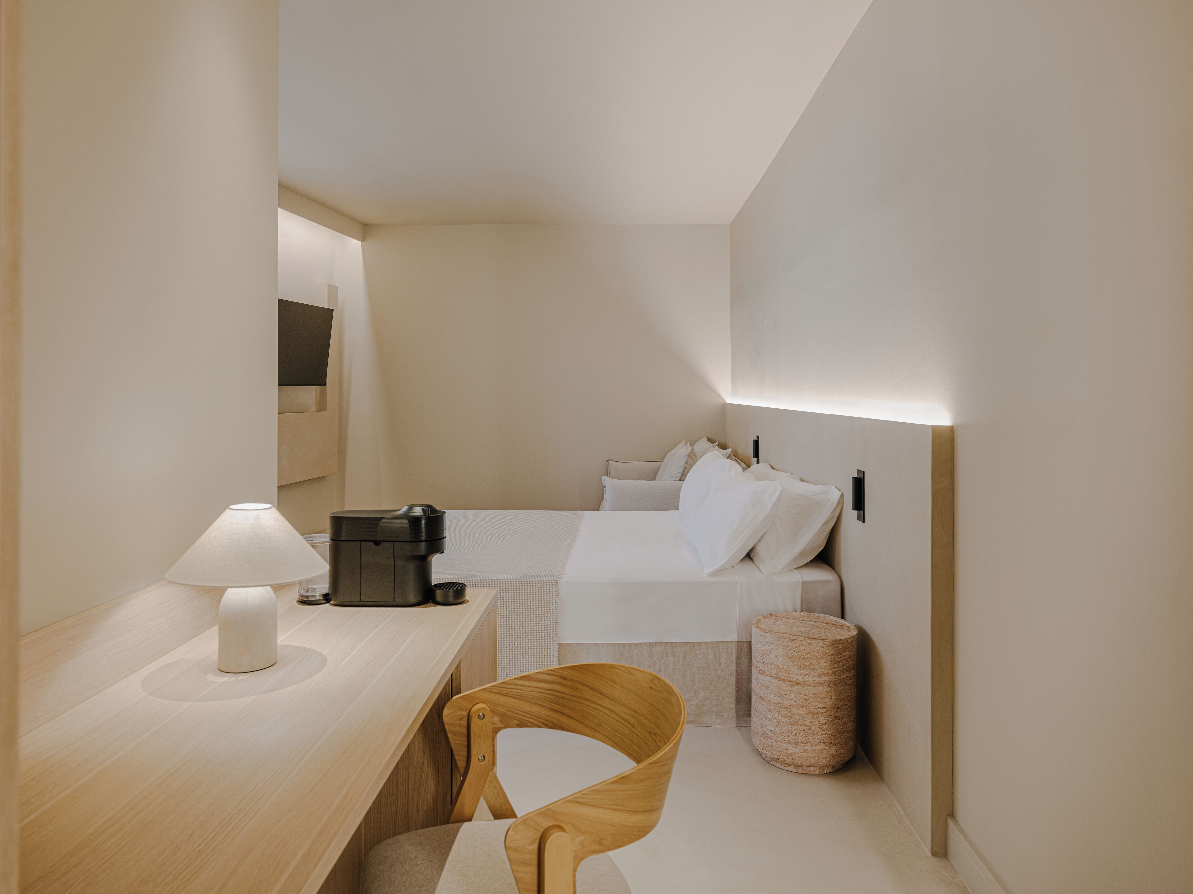 Habitación de hotel compacta con escritorio, silla, cama y un pequeño cubo de basura.