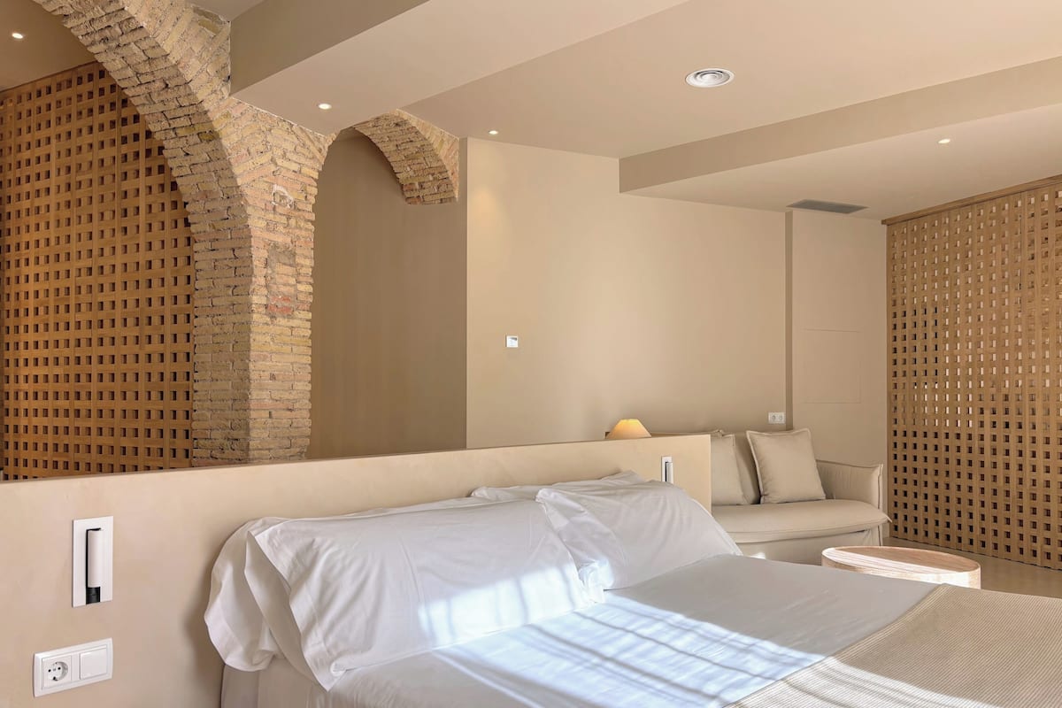 Une chambre à coucher moderne avec un grand lit, une tête de lit en bois, un mur en briques et une cloison en bois.