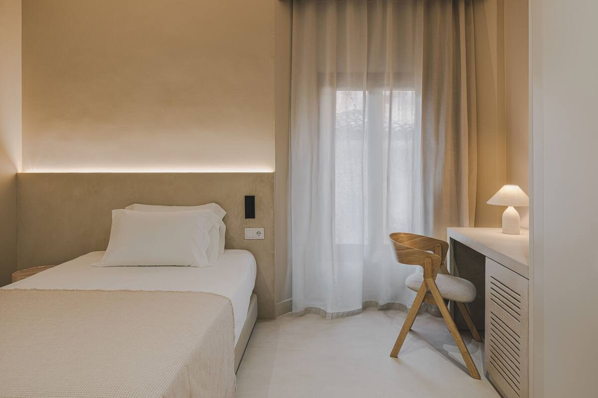 Une chambre d’hôtel avec un lit, une chaise, un bureau et une fenêtre avec des rideaux.