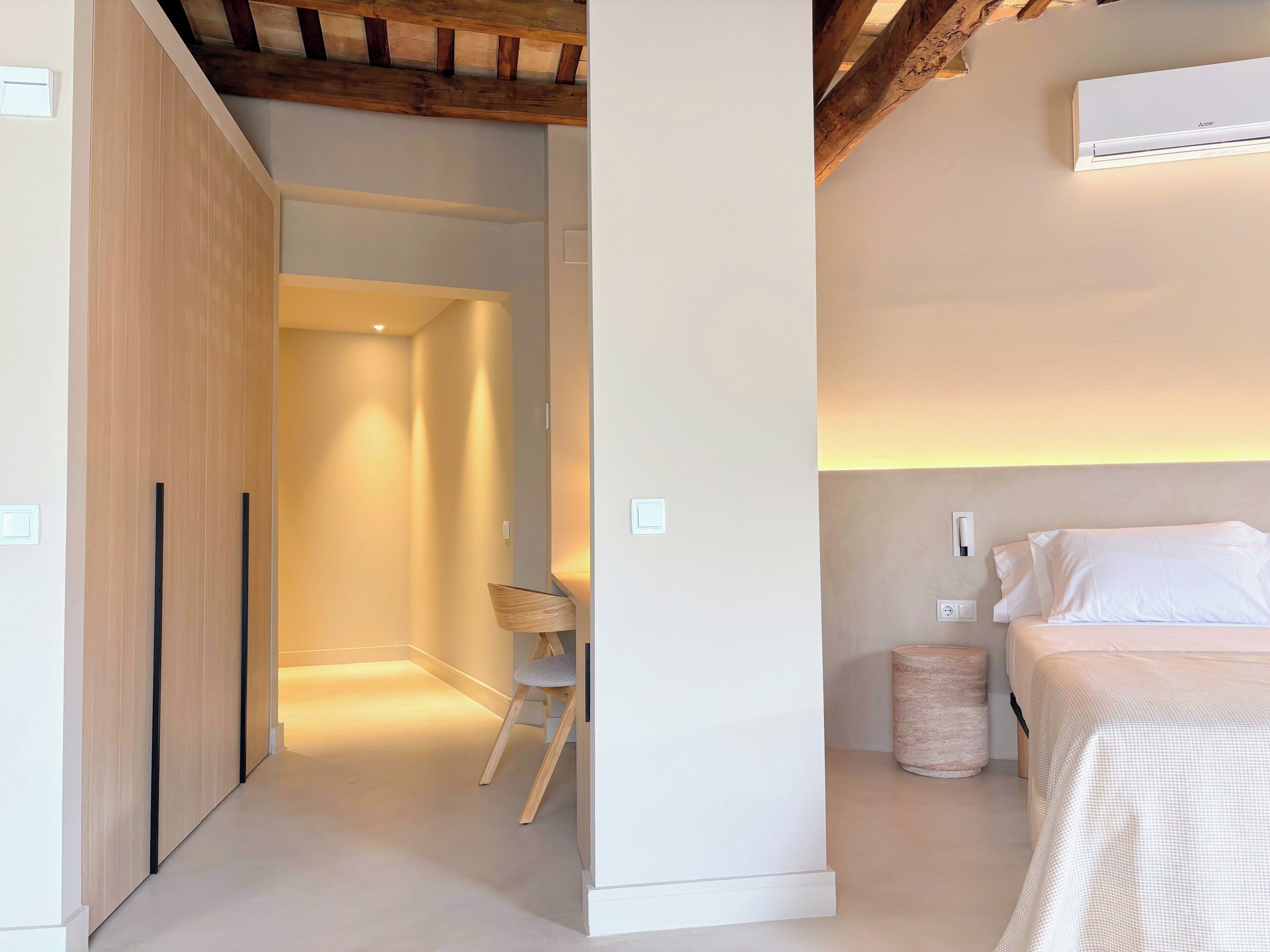 A hotel room with a bed, bedside lamp, and a small seating area with a chair and a basket.