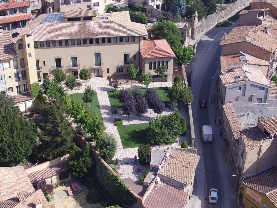 Vista aérea de um bairro residencial com edifícios de telhado de terracota, um pátio central com árvores e uma rua estreita.