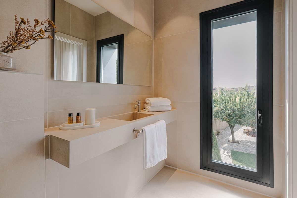 Une salle de bain moderne avec une grande fenêtre, un lavabo équipé de produits de toilette et un miroir.