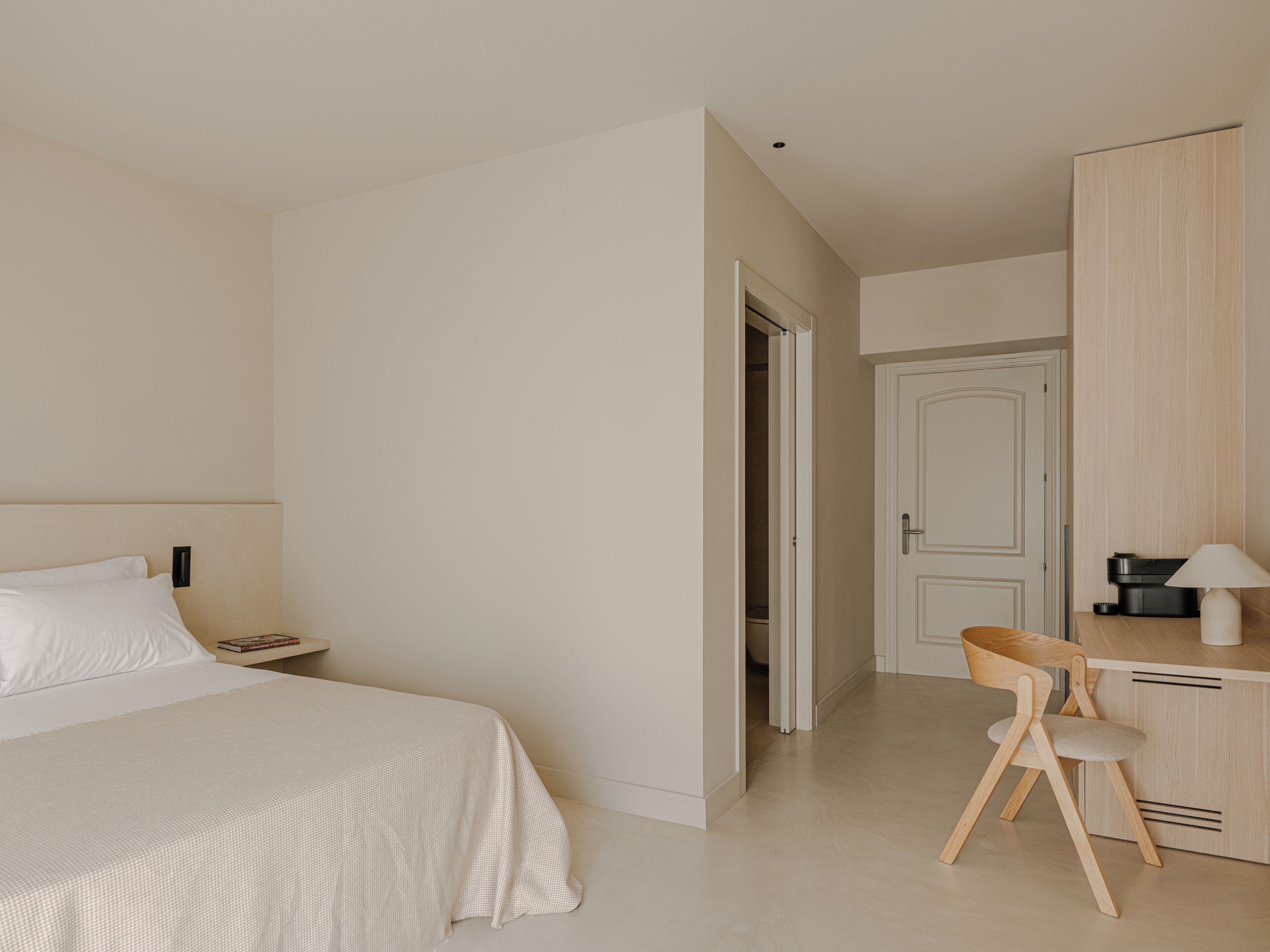 Habitación de hotel minimalista con una cama, un escritorio y una silla.