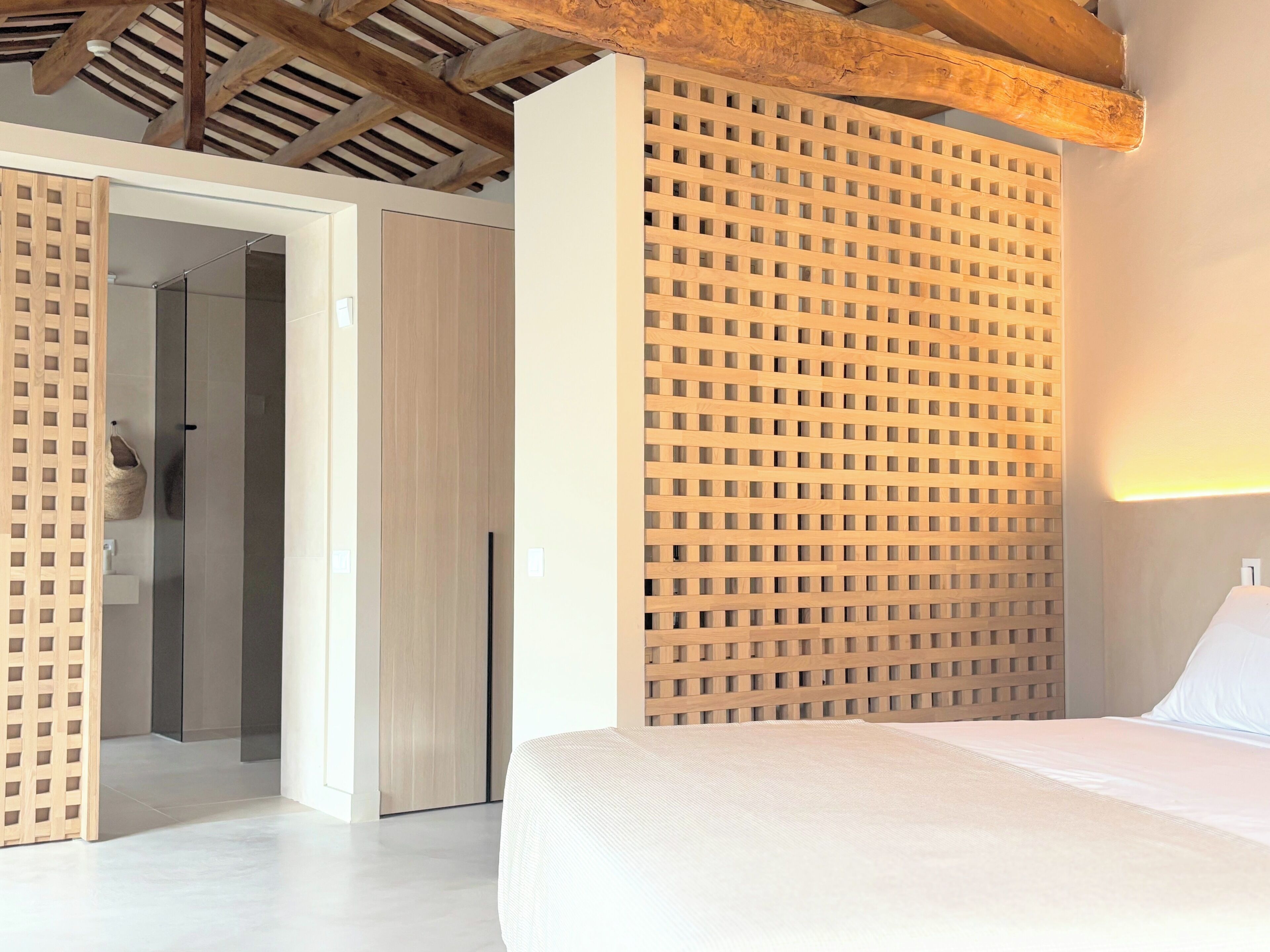 A bedroom with a bed, a wooden headboard, a wardrobe, and a door leading to a bathroom.