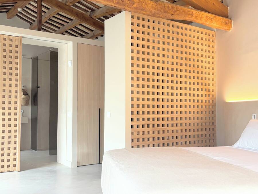 A bedroom with a bed, a wooden headboard, a wardrobe, and a door leading to a bathroom.