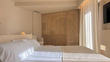 A hotel room with a bed, a wooden partition, a lamp, and a TV mounted on the wall.
