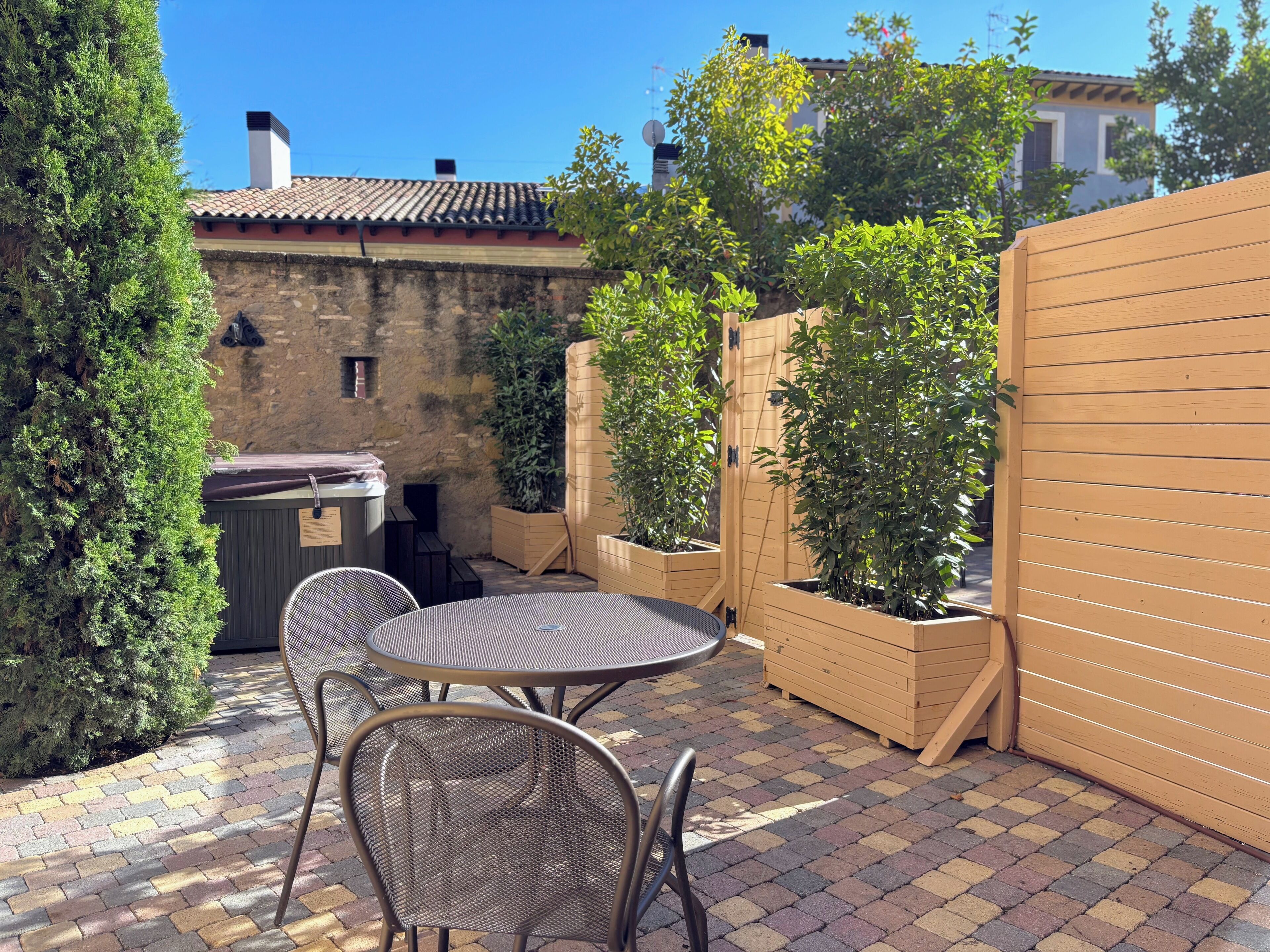 A patio with a round table and two chairs, surrounded by potted plants and a wooden fence.