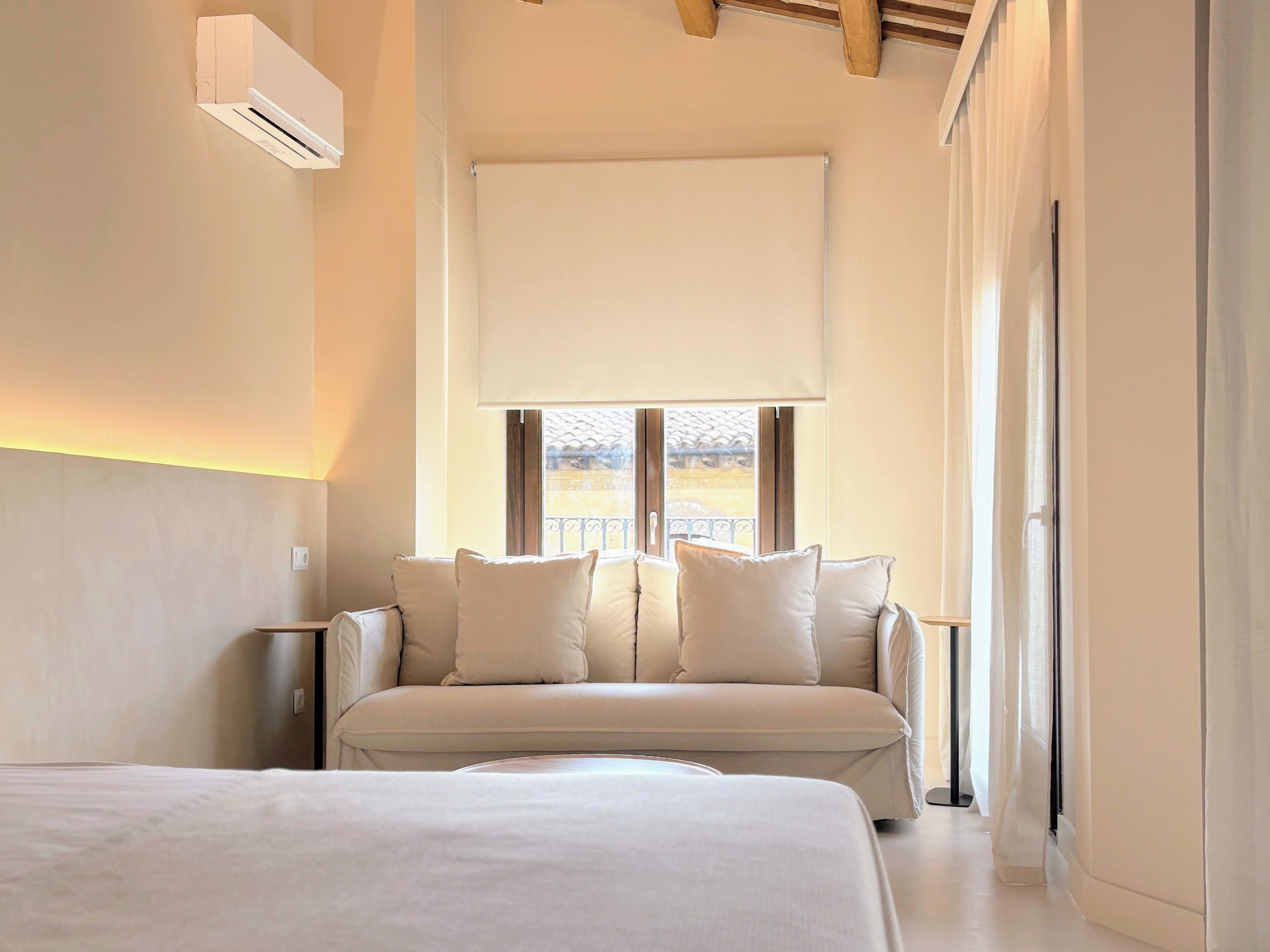 Un dormitorio moderno con una cama grande, un sofá con cojines, una ventana con vistas y un equipo de aire acondicionado.