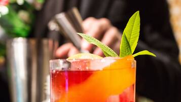 A cocktail with a garnish, a bar area, and a blurred figure in the background.