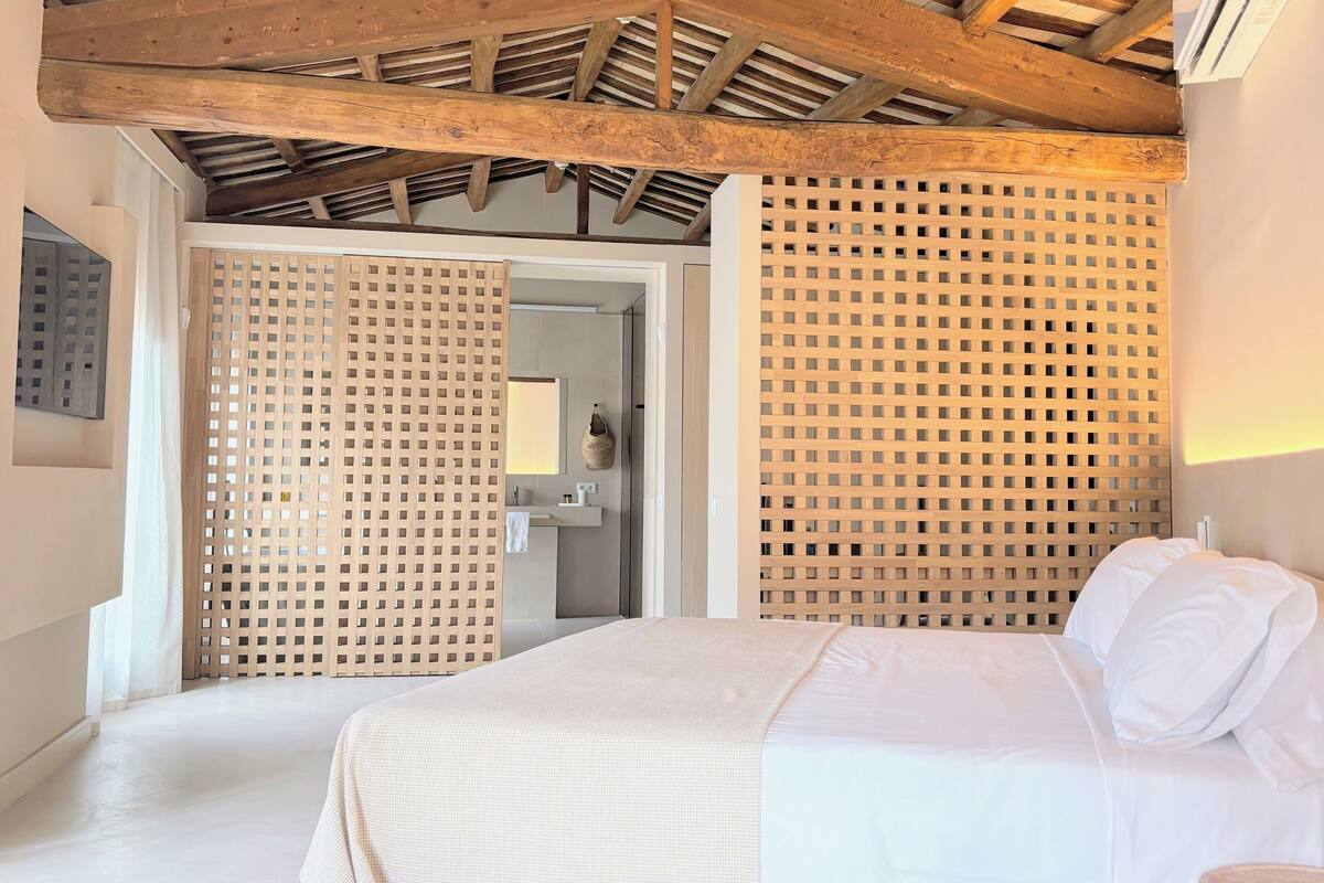 Une chambre avec un plafond en bois, un lit avec une literie blanche et une cloison en bois.