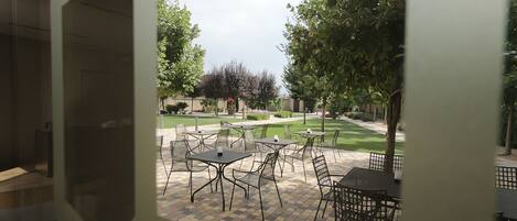 An outdoor patio area with tables and chairs, surrounded by a well-maintained lawn and trees.
