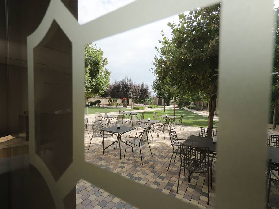 Un patio al aire libre con mesas y sillas, rodeado de un césped cuidado y árboles.