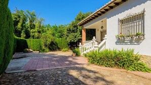 A stone-paved pathway leading to a white building with a tiled roof and a balcony with potted plants. - Casa San Rafael (Navajas)
