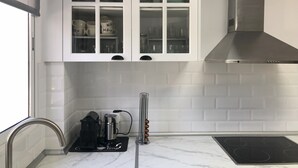 A modern kitchen with white cabinets, a stainless steel range hood, a built-in stovetop, and a coffee machine. - Casa San Rafael (Navajas)