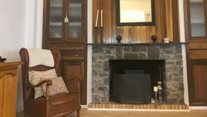 A room with a stone fireplace, wooden cabinets with glass doors, and a chair with a cushion. - Casa San Rafael (Navajas)