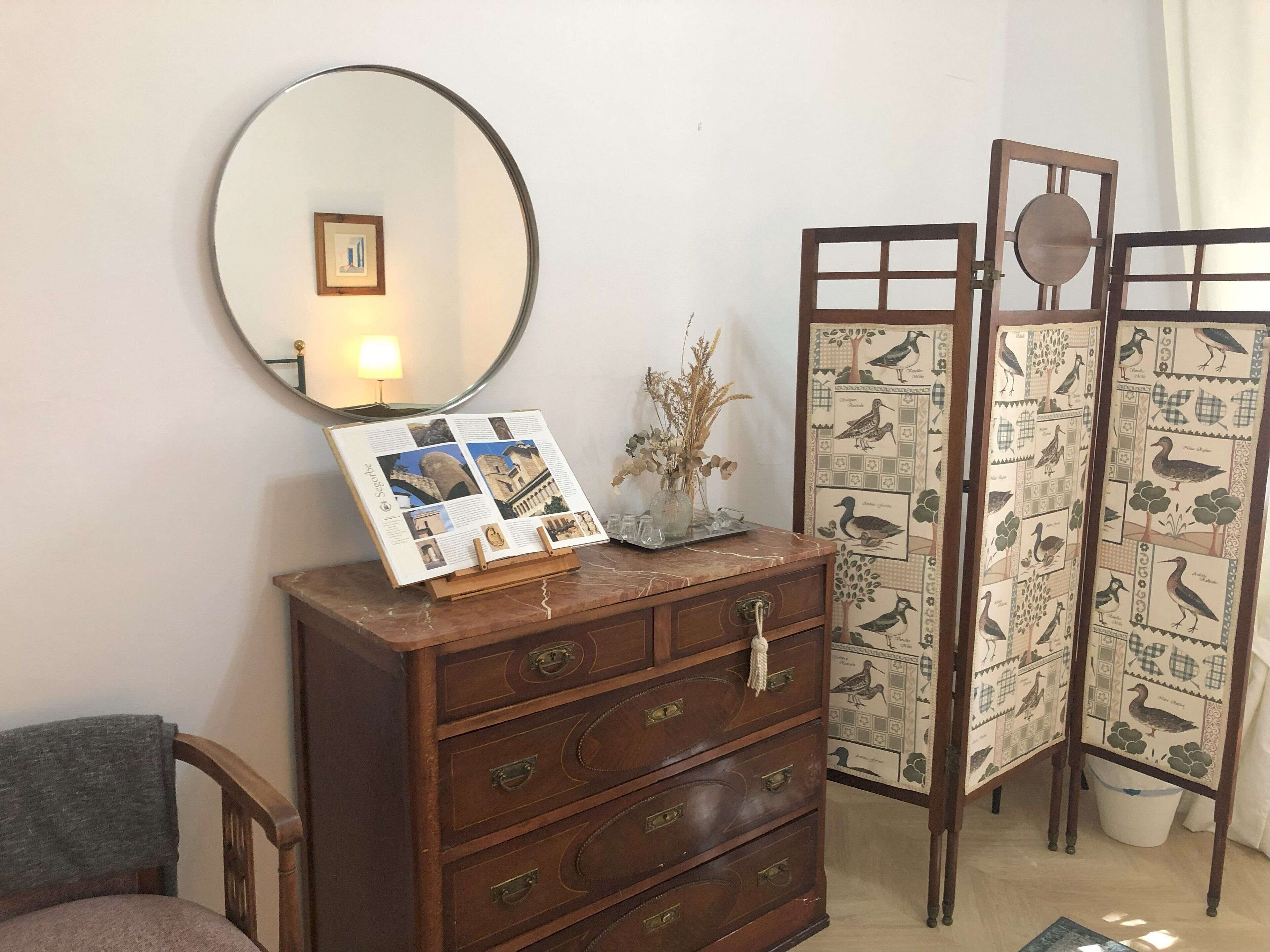 A wooden dresser with a mirror, a framed photo, and a decorative vase with dried plants.