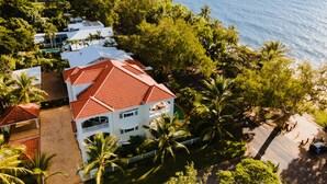 A coastal hotel with a red-tiled roof, surrounded by lush greenery and a view of the sea. - Villa Beach Palm Cove (Clifton Beach)