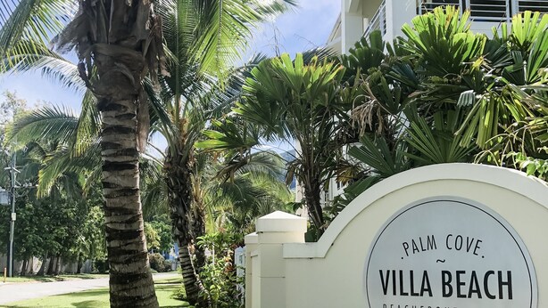 A sign for Villa Beach Beachfront Suites with palm trees and greenery in the background. - Villa Beach Palm Cove (Clifton Beach)