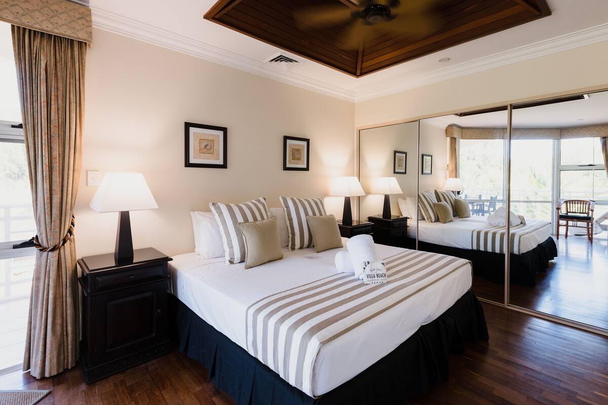 Habitación de hotel con una cama grande, dos mesitas de noche con lámparas, un espejo y vistas al exterior.