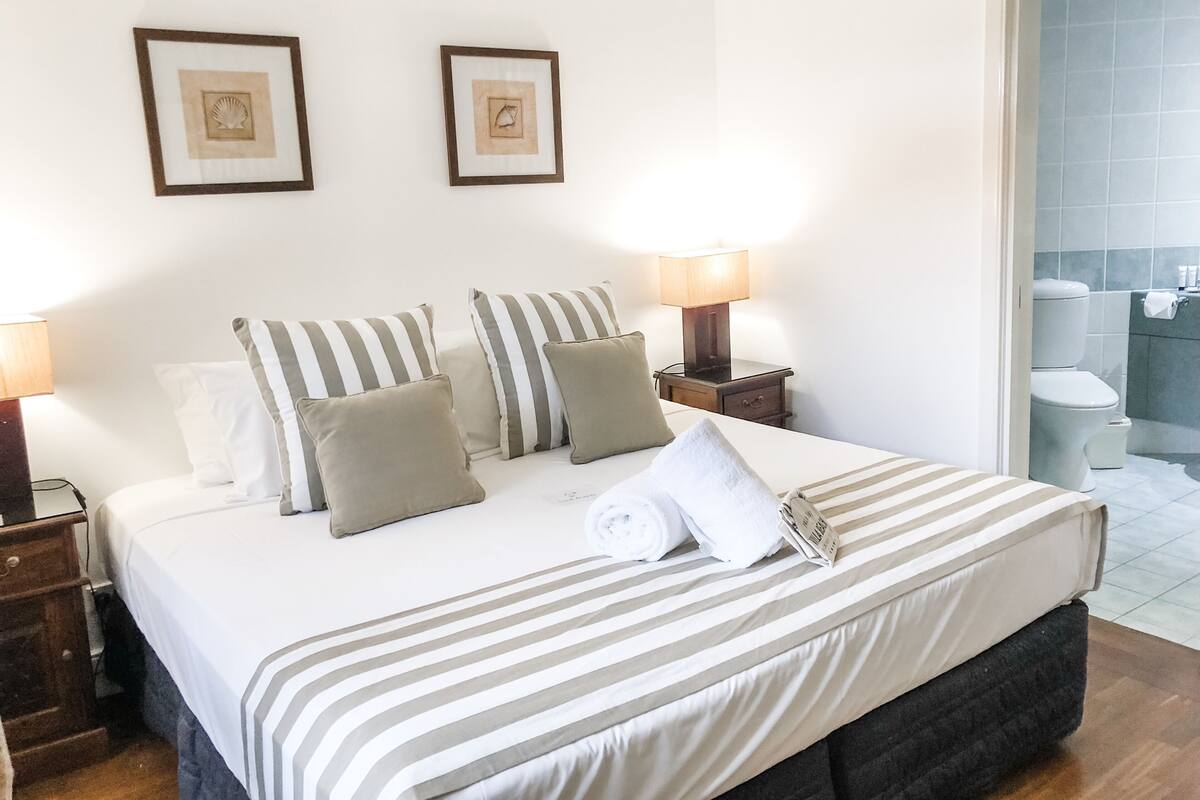 Una cama bien hecha con ropa de cama a rayas, dos lámparas de noche y un cuadro en la pared.
