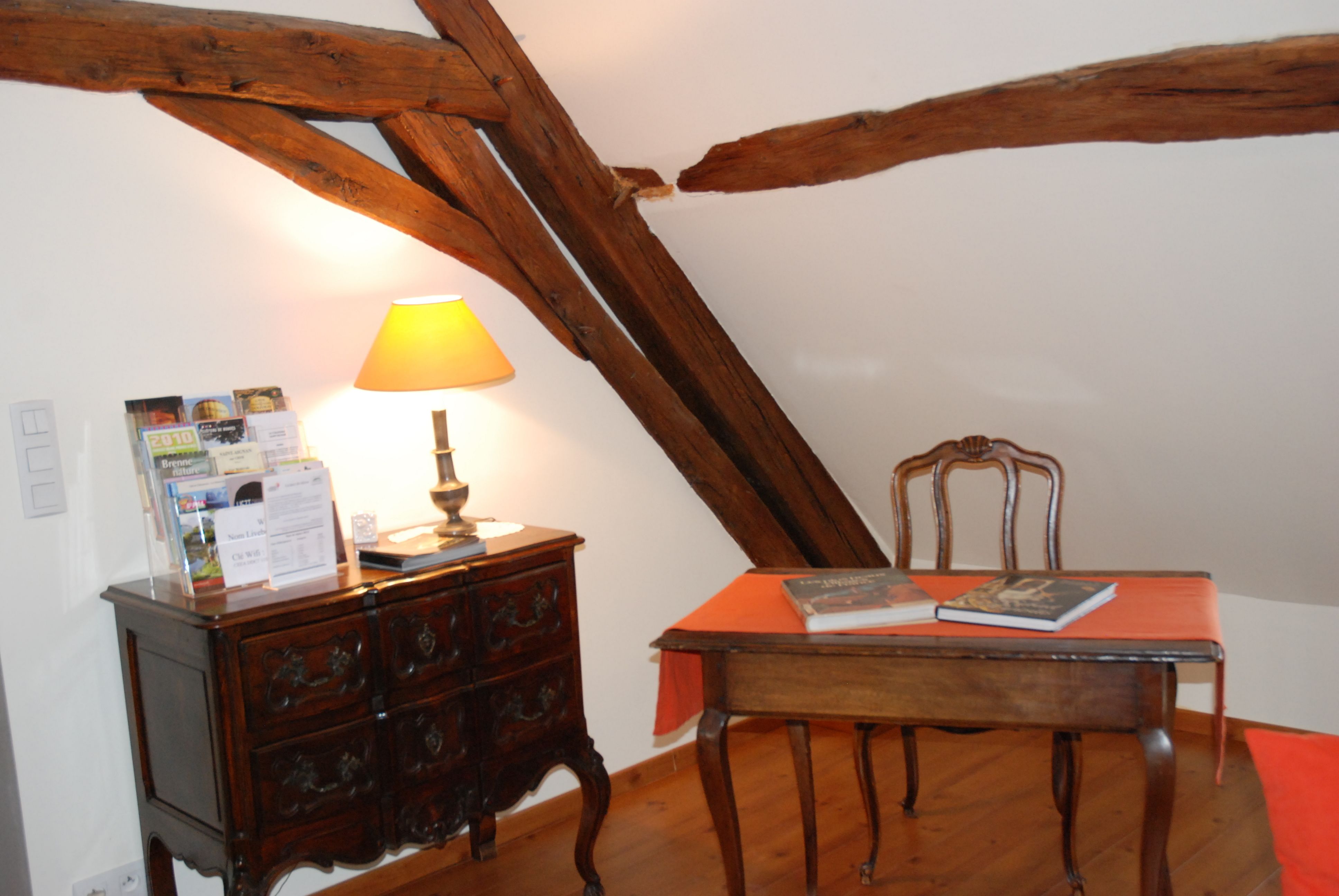 Una habitación con techo de madera, una mesa con una silla, una lámpara y un aparador de madera con cajones.