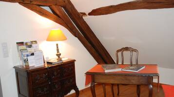 Una habitación con techo de madera, una mesa con una silla, una lámpara y un aparador de madera con cajones.