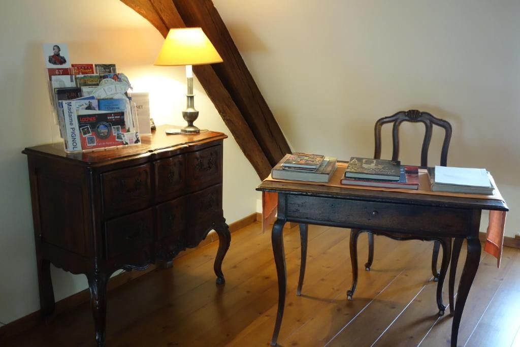 A wooden desk with a lamp, a chair, and a stack of books and magazines.