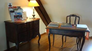 A wooden desk with a lamp, a chair, and a stack of books and magazines.