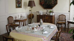 A dining room with a table set for four, surrounded by wooden chairs. A chandelier hangs from the ceiling, and a large painting is on the wall. - Le Fassardy - Chambre d'Hôtes (Chateauroux)