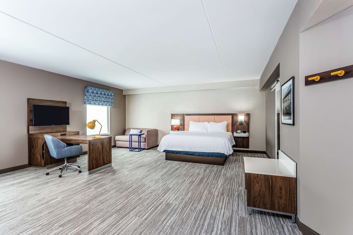 Quarto de hotel com cama, escrivaninha, cadeira e uma pequena mesa.