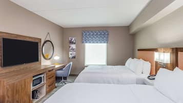 Ein Hotelzimmer mit zwei Betten, einem Fernseher, einem Schreibtisch mit Lampe, einem Sessel und einem Fenster mit Blick.